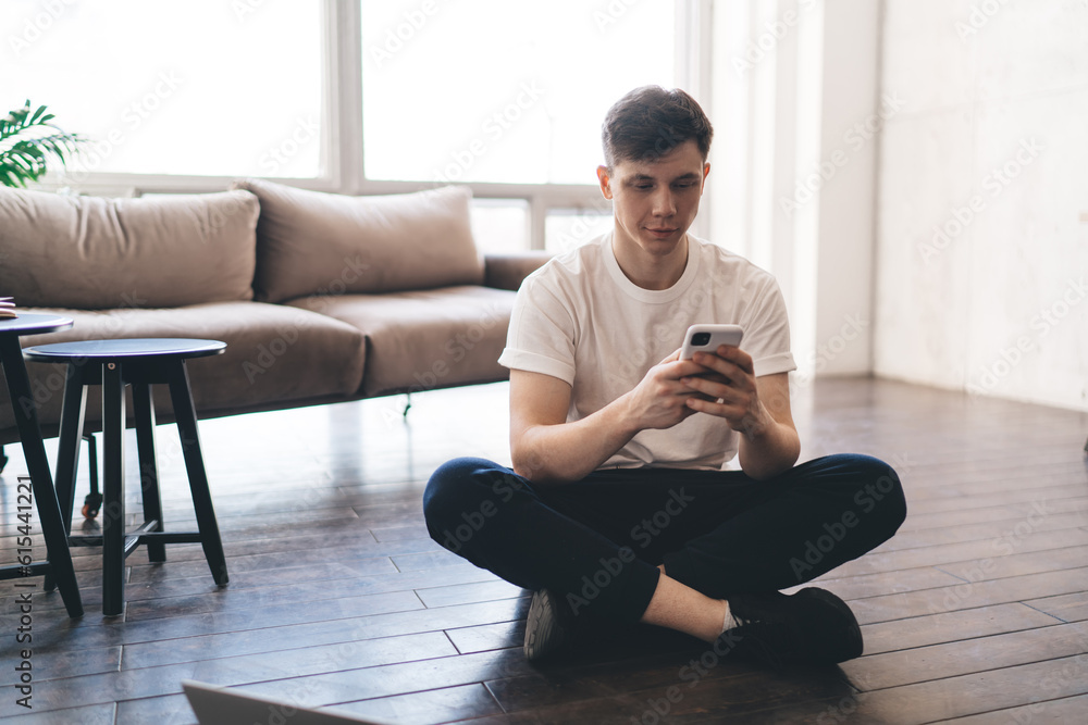 Young man with smartphone sitting on floor at home Young man with smartphone sitting on floor at home
