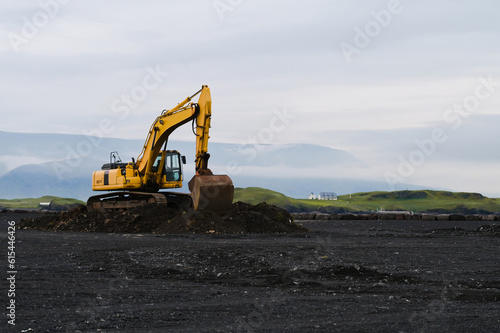 Yellow excavator on black sand against the backdrop of mountains. Construction in Iceland. Beautiful nature