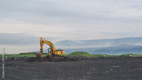 Yellow excavator on black sand against the backdrop of mountains. Construction in Iceland. Beautiful nature
