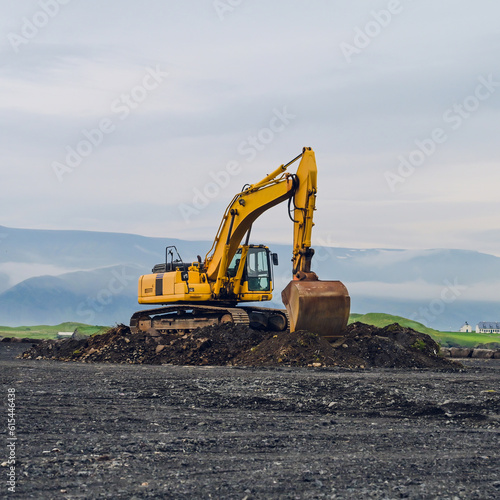 Yellow excavator on black sand against the backdrop of mountains. Construction in Iceland. Beautiful nature