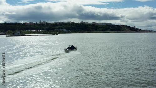 Aerial footage of a man driving a fast motorboat moving along the big Volga River in the Russian city of Nizhny Novgorod, summer nature, a barge floating along the river photo