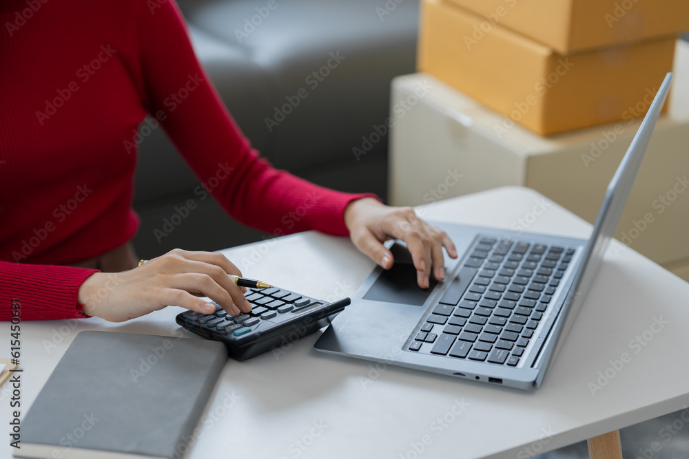 Φωτογραφία female online seller online shop use calculator and a laptop to calculate the cost before packaging e-commerce products
