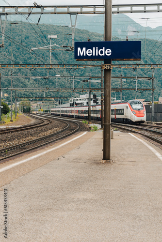 Melide station, blue sign with the name of the station. The high speed train is coming.
