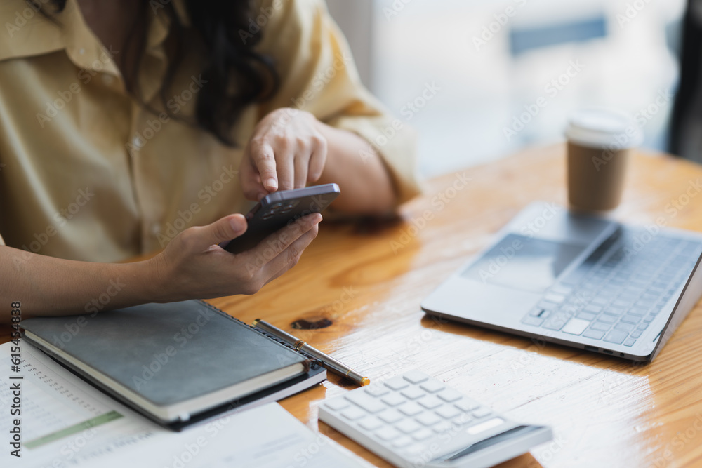 Asian businesswoman using mobile phone to search information and chat via application while sitting at work using laptop with paperwork making plan, investing, analyzing financial report. Asian businesswoman using mobile phone to search information and chat via application while sitting at work using laptop with paperwork making plan, investing, analyzing financial report.