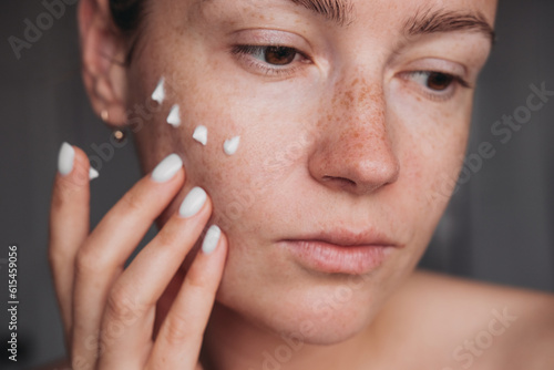 Wallpaper Mural Young woman applying dots of face cream on her cheek, close up portrait  Torontodigital.ca