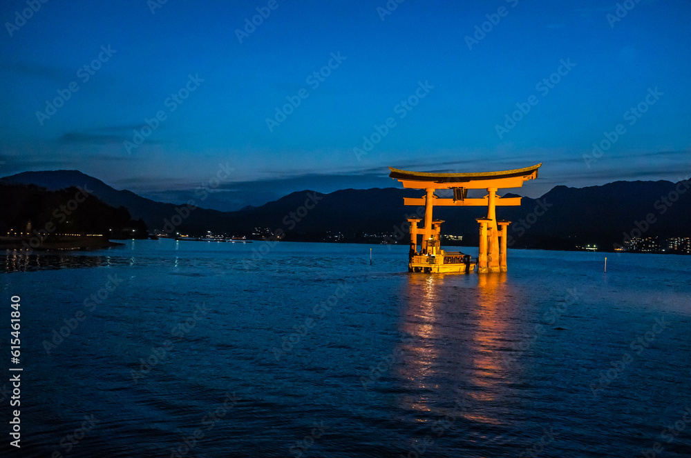 日本の広島県にある日没後の海に浮かぶ厳島神社の鳥居と小船