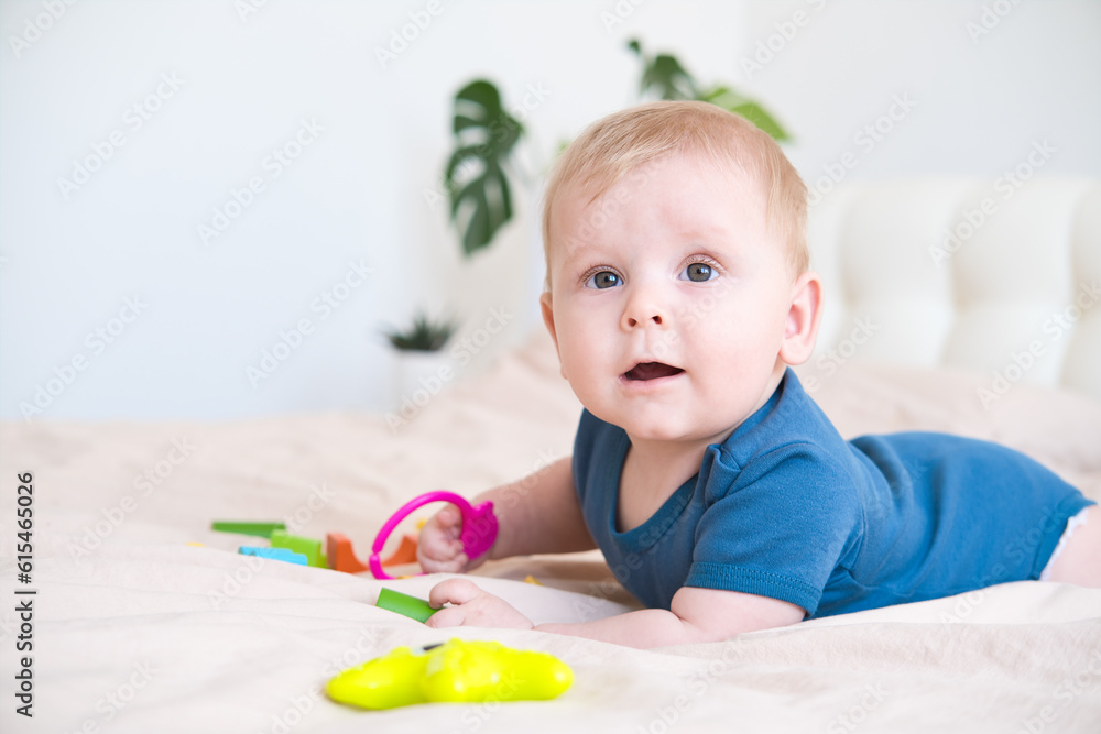 baby boy in blue bodysuit playing with colorful plastic toys on bed