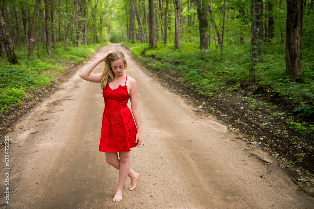 Teenage girl in red dress and barefoot on a dirt road in a wood land area; Walker, Minnesota, United States of America Teenage girl in red dress and barefoot on a dirt road in a wood land area; Walker, Minnesota, United States of America