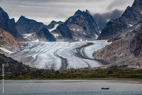 View of glacier flowing through the mountain peaks at the Southern tip of Greenland with silhouette of a boat passing by in the grey waters of Prins Christian Sund; Southern Greenland, Greenland photo