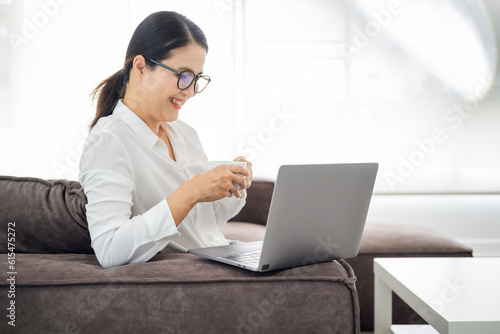 Nice beautiful mature lady with black hair work at the notebook sit down on the sofa at home - check on oline shops for cyber monday sales - technology woman concept for alternative office freelance. photo