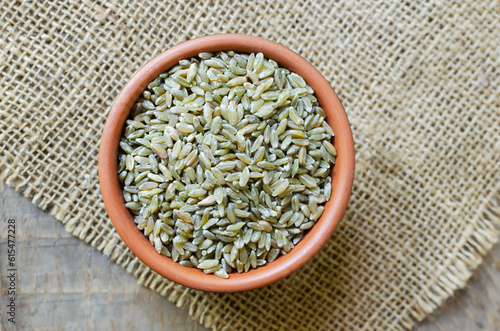 Raw freekeh or firik in ceramic bowl on burlap on wooden background. Concept of healthy food. Vegan and vegetarian food. Horizontal orientation. Top view. photo