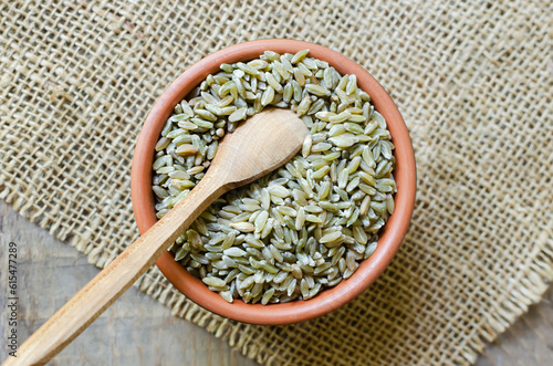 Raw freekeh or firik in ceramic bowl with spoon on burlap on wooden background. Concept of healthy food. Vegan and vegetarian food. Horizontal orientation. Top view. photo