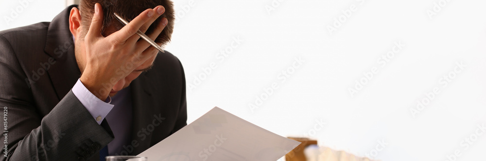 Naklejka premium Stressed businessman with headache or migraine working at office desk. Bankruptcy depression and loan documents with debts