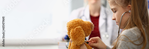 Photos Girl child with stethoscope listens to toy in background sits doctor