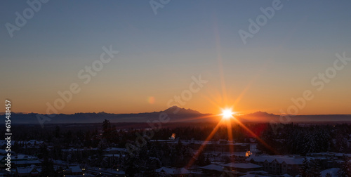 Sunburst over mountains and cityscape at sunset; Surrey, British Columbia, Canada photo