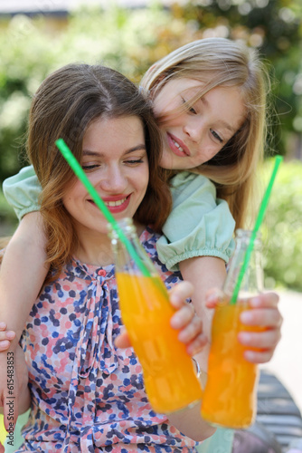 Happy pastime mom and daughter drink soda with straws in the park.