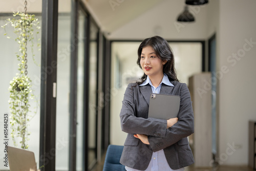Portrait of beautiful asian business woman confident standing in office and holding laptop.