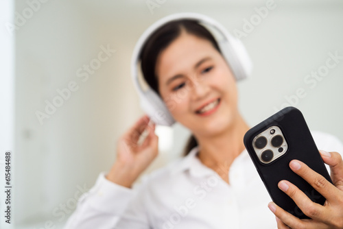 Smiling asian young woman listening to the podcast e-book music song singer rock band in headphones earphones, choosing sound track on cellphone isolated on sofa couch in living room