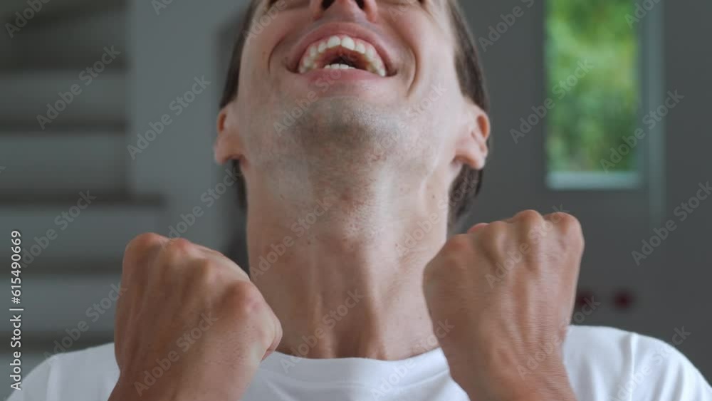Close up portrait of happy young man 30s wears white t-shirt look camera celebrate win scream rejoices doing winner hands gesture isolated standing at home. Male winner clenching fists say yes. Close up portrait of happy young man 30s wears white t-shirt look camera celebrate win scream rejoices doing winner hands gesture isolated standing at home. Male winner clenching fists say yes.