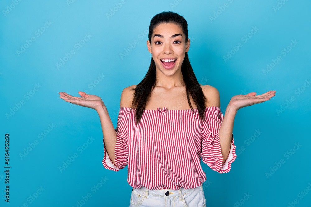 Photo of funky excited girl dressed off shoulders striped blouse comparing arms empty space isolated blue color background Photo of funky excited girl dressed off shoulders striped blouse comparing arms empty space isolated blue color background
