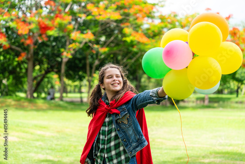 smiling  happy eight-year-old girl wearing a red shawl holding colorful balloons was running around in the park.