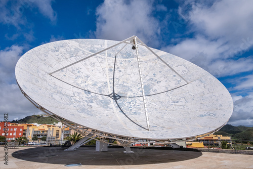 View of a large satellite dish to observe the cosmos  decorated with the lunar topography  with large white clouds in the background.