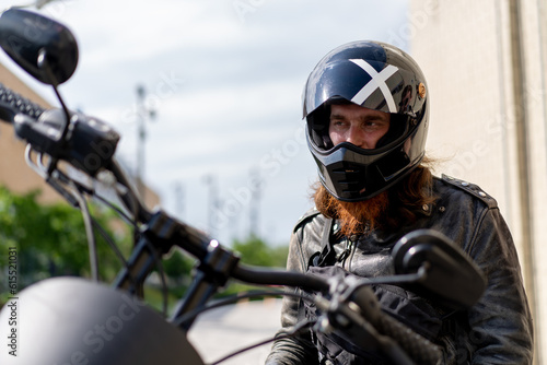 brutal red bearded biker sitting on a black motorcycle after a race in a helmet thirst for speed motorsport concept