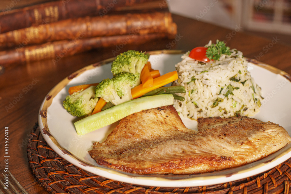 Beautiful plate of grilled fish with rice. In the background old books Beautiful plate of grilled fish with rice. In the background old books