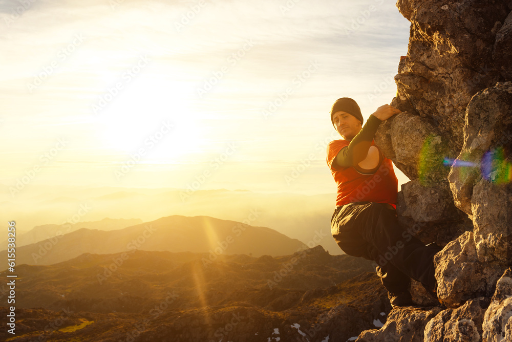 white man with wool cap and tattoos climbing a mountain at sunset. extreme sport and outdoor activities.