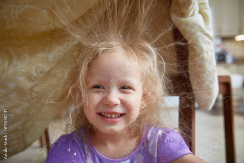 Static electricity electrified the hair of a little girl sitting under a synthetic blanket.