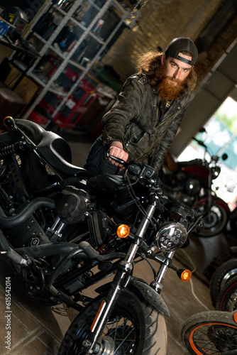 Creative authentic motorcycle workshop Garage redhead bearded biker mechanic standing near motorcycle checking it