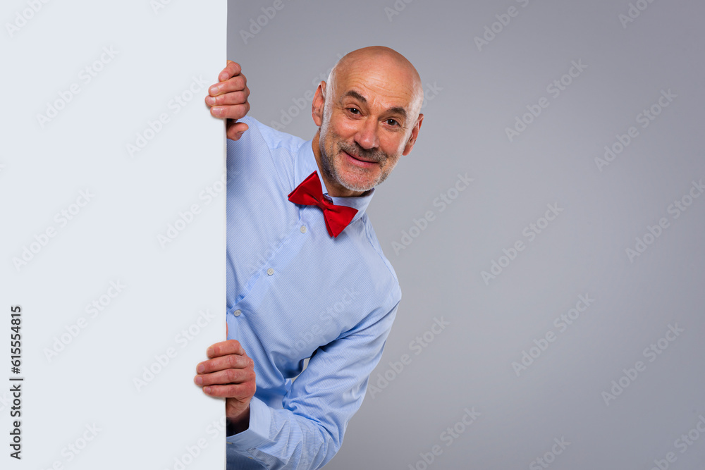 Amazed face man wearing bow tie and looking out of white board while standing at isolated background Amazed face man wearing bow tie and looking out of white board while standing at isolated background