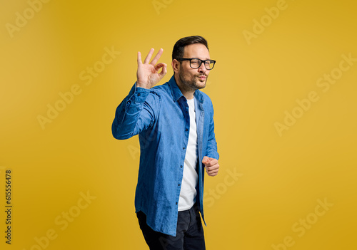 Fotografi Happy businessman puckering lips and gesturing OK sign while standing against ye