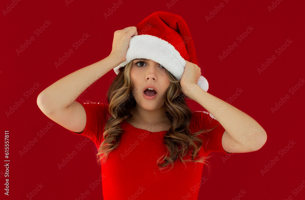 Young beautiful brunette girl in red dress and christmas hat shocked over red background. Young beautiful brunette girl in red dress and christmas hat shocked over red background.