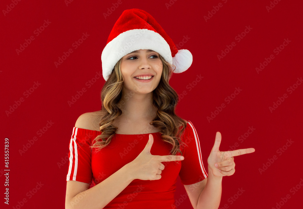 Smiling young Santa woman in red dress, Christmas hat pointing index fingers aside on mock up copy space isolated on red background, studio portrait. Happy New Year celebration merry holiday concept