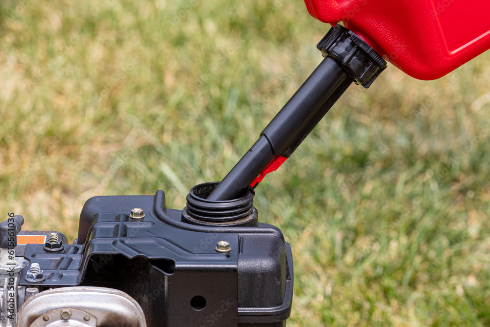 Gas can pouring gasoline into fuel tank of lawnmower. Lawn equipment