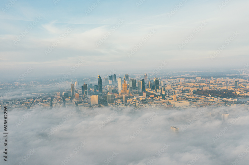 Drone flies towards the urban landscape with buildings in the fog at sunrise. Aerial view of cityscape in the fog at sunrise. Warsaw Poland.