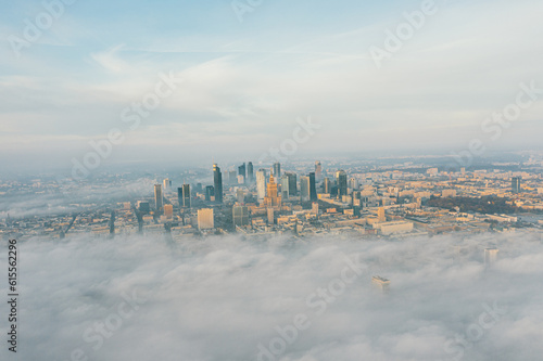 Drone flies towards the urban landscape with buildings in the fog at sunrise. Aerial view of cityscape in the fog at sunrise. Warsaw Poland.