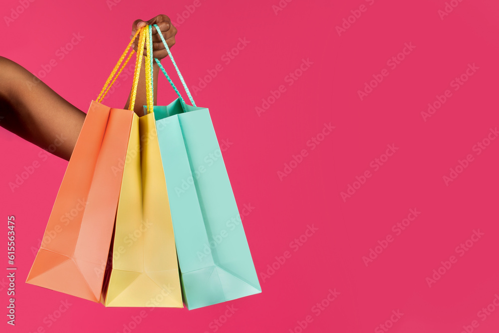 Hand of young black lady shows many packages with purchases, isolated on pink background