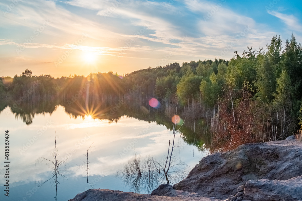 Fototapeta premium Beautiful landscape with colorful sunset over forest lake, Epic red and golden clouds above the forest lake at sunrise. Dramatic cloudscape. Symmetry reflections on the water, natural mirror. Idyllic