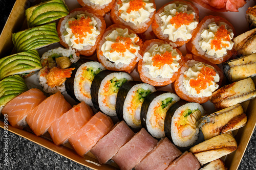 Set of sushi rolls with salmon, avocado, smocked eel, tobiko caviar in transport box on black background