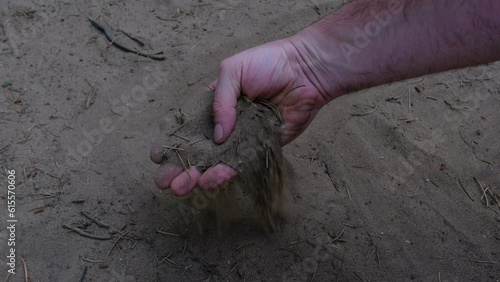Slow motion and close up while taking handful of dry soil or dirt from uncultivated land and sifting through fingers in shadow.