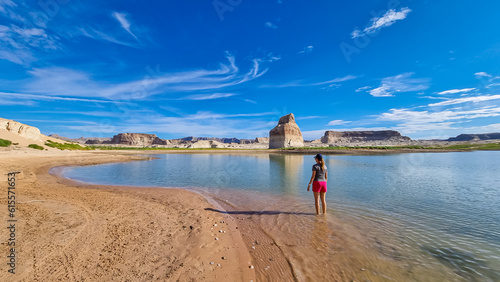 Photography Rear view of woman walking at lakeshore looking at solitary rock formation Lone Rock in Wahweap Bay at Lake Powell, Glen Canyon Recreation Area, Page, Utah, USA
