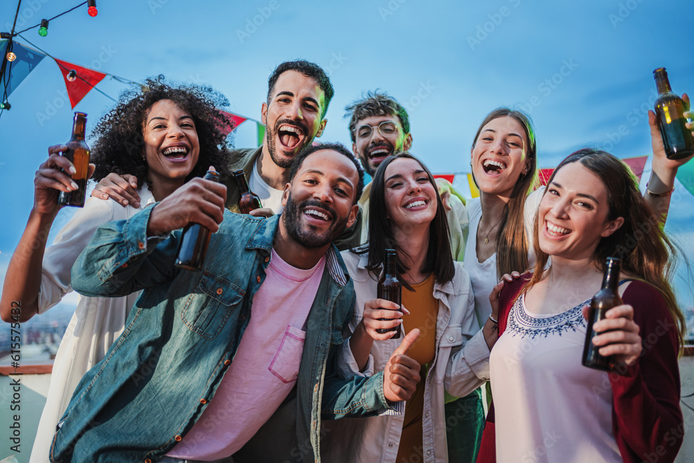 Fototapeta premium Group of cheerful best friends on a rooftop wine party. Crowd of young people drinking, toasting glasses, laughing and having fun on a friendly meeting, enjoying happy hour at winery bar restaurant
