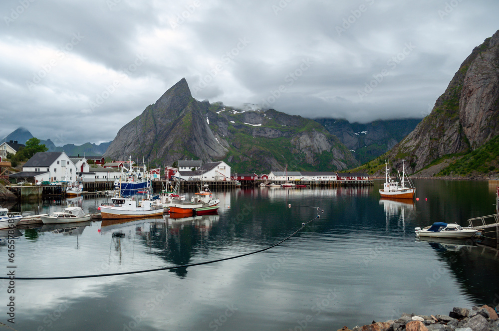 A bay between mountains with moored fishing boats and wooden houses in the background - Svolvaer, Norway
