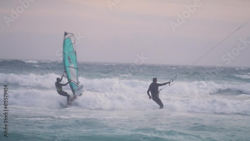 A wind surfer and a kite surfer surfing on the ocean together at susnet