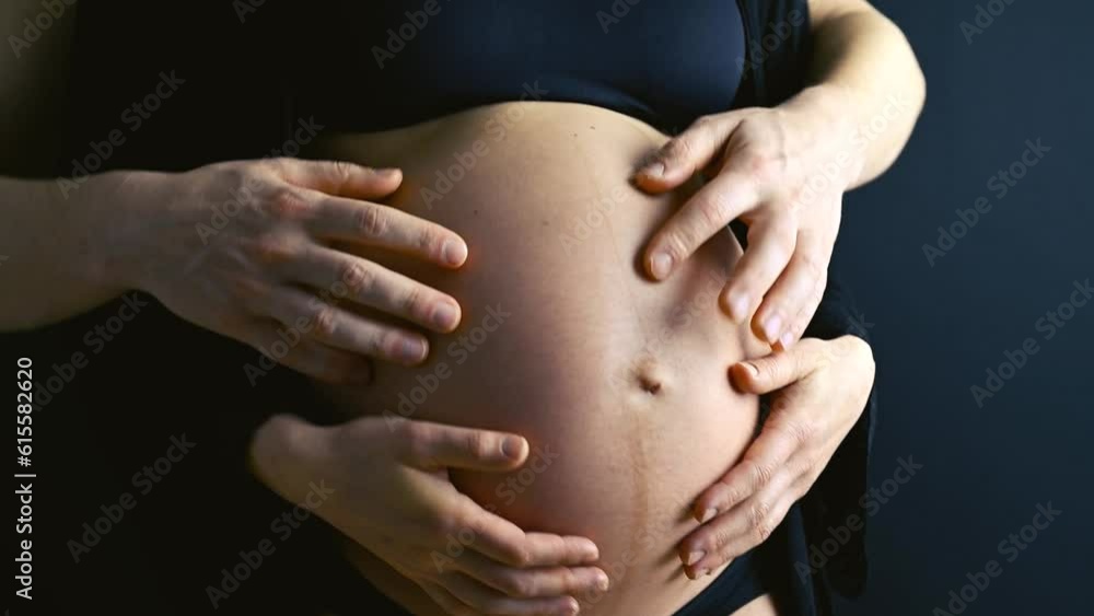 Closeup of pregnant mother's naked round belly in underwear, joined by father's playful hands. Last month of pregnancy - 36th week. Side view. Black background. Closeup of pregnant mother's naked round belly in underwear, joined by father's playful hands. Last month of pregnancy - 36th week. Side view. Black background.