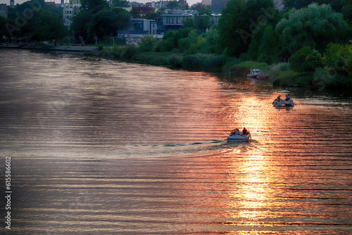 Zachód słońca nad wodą płynie łódka z ludźmi. 