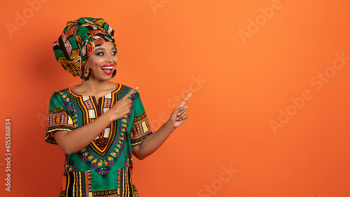 Excited beautiful black woman pointing at copy space on orange
