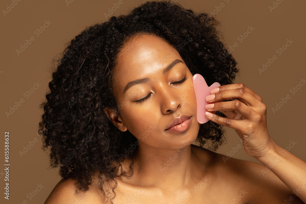 © Prostock-studio - Joyful pretty african woman using gua sha stone, massaging face